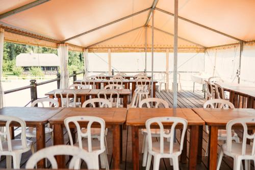 une grande tente avec des tables en bois et des chaises blanches dans l'établissement Caravans Camping in Young Riders School, à Inčukalns