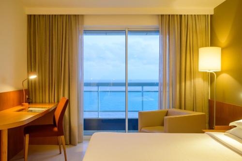 a hotel room with a bed and a desk and a window at Hotel Luzeiros São Luis in São Luís