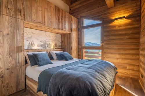 a bedroom with wooden walls and a bed with a window at Chalet La Tribu du Danay, neuf, 12 personnes in Saint-Jean-de-Sixt