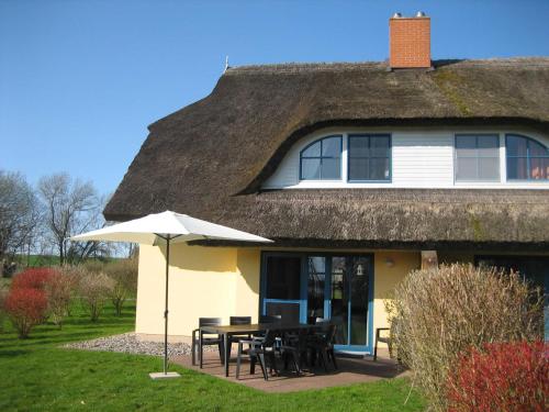 ein Haus mit einem Strohdach mit Tischen und einem Regenschirm in der Unterkunft Komfortables Reetdachferienhaus Hasel 1 in Puddemin