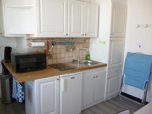 une cuisine avec des armoires blanches, un évier et un micro-ondes dans l'établissement Cambuse Appartement à Sangatte au premier étage à 50 metres de la plage, à Sangatte