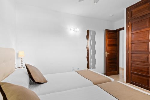 a bedroom with a white bed and a wooden door at Paloma Beach Apartments in Los Cristianos
