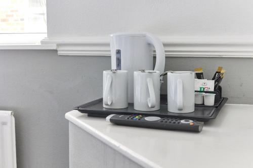 a tray with three white mugs and a remote control at Properties Unique Dene Rooms - Family Room in Newcastle upon Tyne