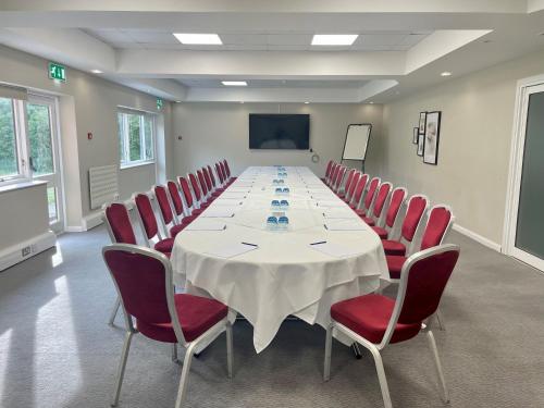 a conference room with a long table and red chairs at Delta Hotels by Marriott Milton Keynes in Milton Keynes