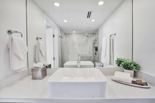 a white bathroom with a large sink and a mirror at Feels Like Summer ~ Panoramic Water Views! in Miami