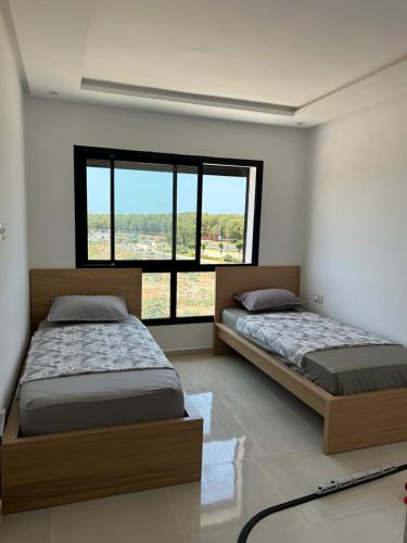 a bedroom with two beds and a large window at شقة مفروشة بالمسبح و نادي رياضي in Kenitra