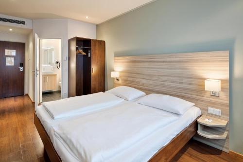 1 dormitorio con 1 cama blanca grande y cabecero de madera en Austria Trend Hotel Salzburg Messe, en Salzburgo