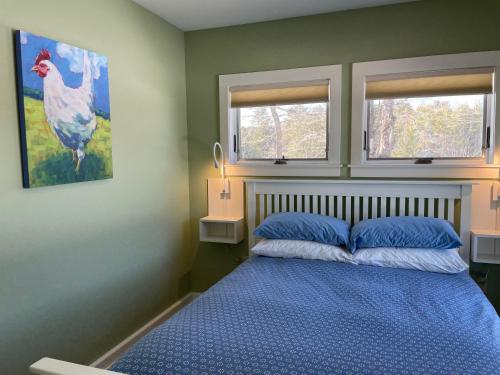 a bedroom with a bed with blue sheets and two windows at Fat Sheep Farm & Cabins in Windsor