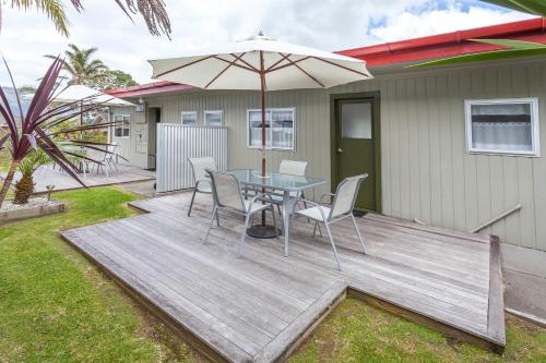 a wooden deck with a table and an umbrella at Tairua Shores Motel in Tairua