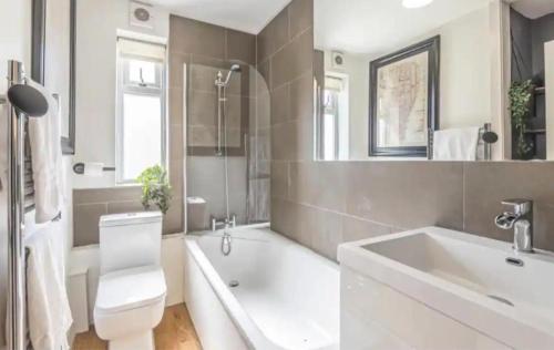 a bathroom with a tub and a toilet and a sink at Egham Contemporary Stylish Three Bedroom Apartment in Egham