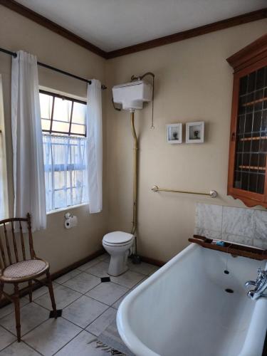 een badkamer met een bad, een toilet en een raam bij La Provence Accommodation in Bloemfontein