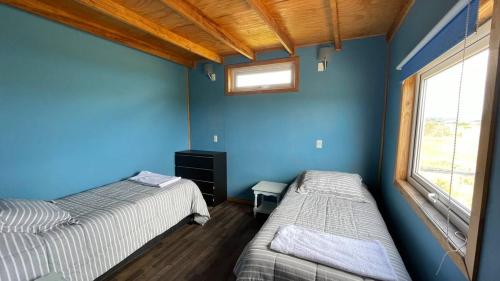 two beds in a room with blue walls and a window at Casa en la Playa in Ancud
