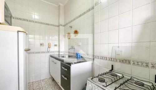 eine weiß geflieste Küche mit einem Herd und einer Spüle in der Unterkunft Apartamento com piscina 1 quarto de até 6 pessoas - Guarujá in Guarujá