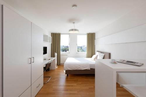 a white bedroom with a bed and a desk at Brera Serviced Apartments Nürnberg in Nuremberg