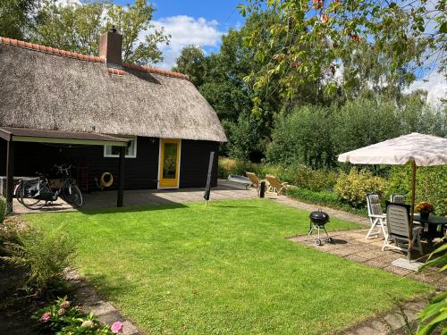 a house with a thatch roof with a grill and a grass yard at Oasis holiday home in Giethoorn next to canal, boat extra in Giethoorn