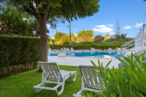 two white chairs sitting in the grass near a pool at T2 Maralvor in Alvor