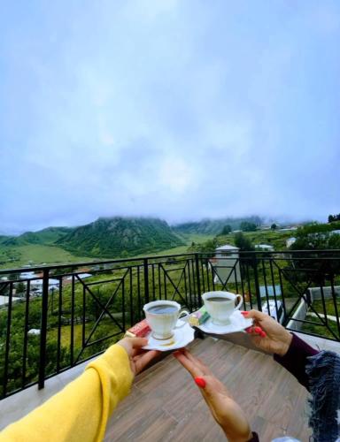 a person holding two cups of coffee on a balcony at Orophile guest house in Gorists'ikhe