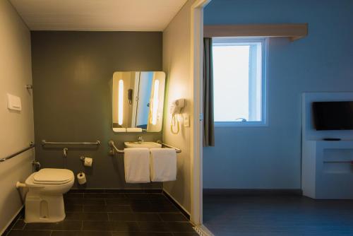 a bathroom with a toilet and a sink and a window at Ibis Guaratingueta Aparecida - Circuito da Fé in Guaratinguetá