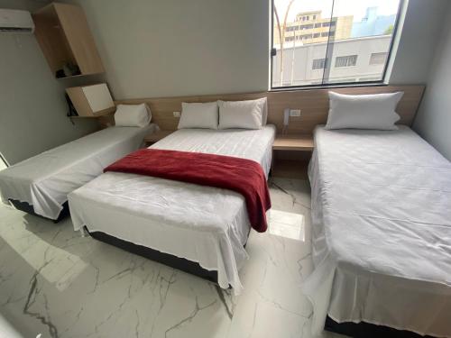 a room with three beds with white sheets and a red blanket at Hotel Fênix Belenzinho in Sao Paulo
