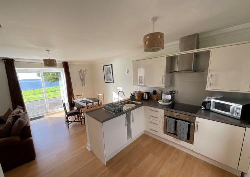a kitchen with white cabinets and a living room at Bracken Cottage in Killean
