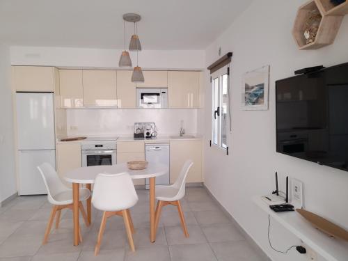 una cocina con mesa y sillas y una cocina con armarios blancos. en Bungalow Paseo del Mar- PLAYA ROCA Residence sea front access - Free AC - Wifi, en Costa Teguise