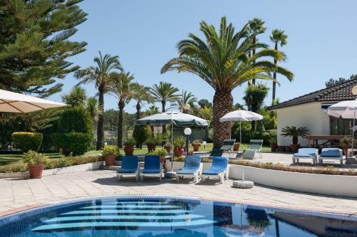 a pool with chairs and umbrellas and palm trees at Villa das Palmeiras in Charneca