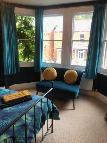 a bedroom with a bed and a blue couch and windows at Balcarres, Rodborough Avenue in Stroud