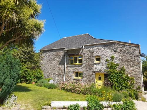 uma casa de pedra com uma porta amarela num quintal em The Barn em Saltash