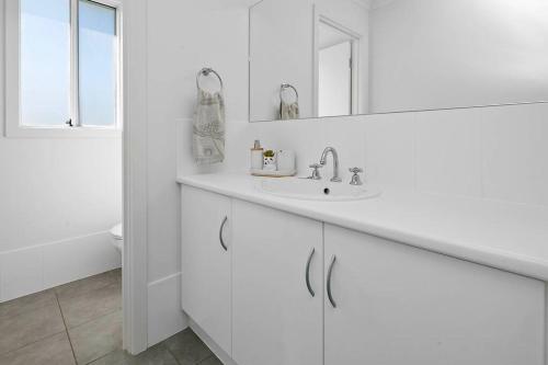 Baño blanco con lavabo y espejo en Harvey Haven -Sleeps upto 15 4 Bdrm 2 5 Bth, en Aldinga Beach