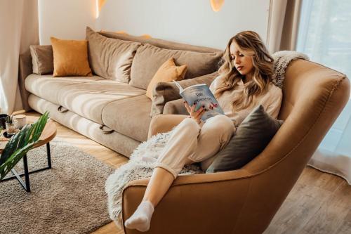 uma mulher sentada num sofá a ler um livro em Apartman WHITE em Divčibare