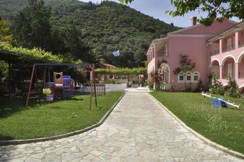 a garden with a playground in front of a pink building at Hotel Elena Ermones in Ermones