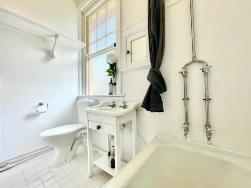 La salle de bains blanche est pourvue d'une baignoire et de toilettes. dans l'établissement Violet's Maison, à Katoomba