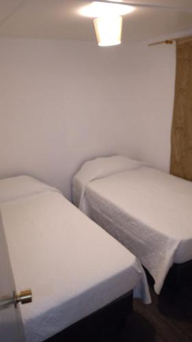 two beds in a small room with white sheets at Casa Paso Jama in San Pedro de Atacama