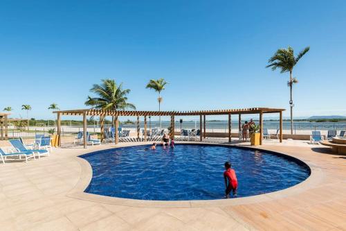 a person standing in a swimming pool next to the beach at Arraial Golden Lake Residence in Arraial do Cabo