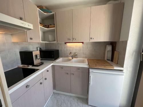 une cuisine avec des armoires blanches, un évier et un micro-ondes dans l'établissement Appartement 2 pièces 4 couchages, terrasse, proche plages - FR-1-226B-172, à Cavalaire-sur-Mer