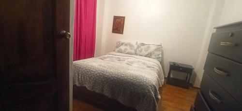 a small bedroom with a bed and a pink curtain at Departamento Emily in Cuenca