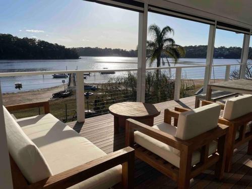 a porch with chairs and a view of a beach at The Sandbar House, Royal National Park, waterfront beach house in Maianbar
