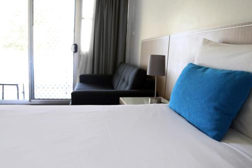 1 dormitorio con cama con almohada azul y sofá en Zorba Waterfront Motel, en Batemans Bay