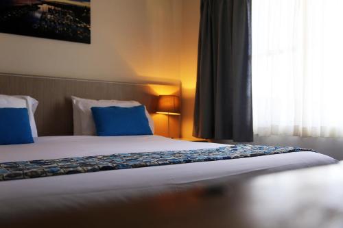 a bedroom with a bed with blue pillows and a window at Zorba Waterfront Motel in Batemans Bay