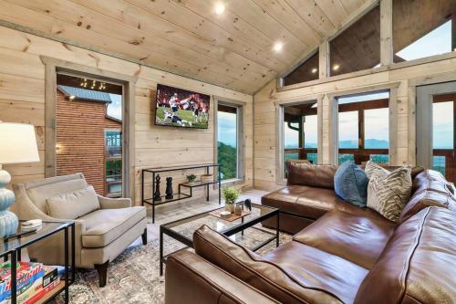 a living room with leather furniture and windows at New Luxury Cabin with Stunning MountainVIEWS,HotTub, FirePit, FirePlace,2 KingBeds, 2 CoveredDecks,BBqGrill, ShuffleBoard and Pool Access in Sevierville