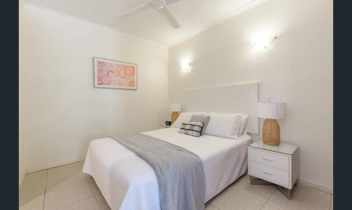 a white bedroom with a bed and a night stand at Charming 1 bedroom Apt - Close to Town & Beach in Port Douglas