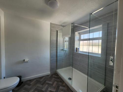 a bathroom with a shower and a toilet and a window at Kennedy Villa - 5 Bed House with Hot Tub in Bicester