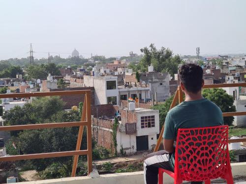 a man sitting in a red chair looking at a city at Sunrise Homestay Agra Near Taj Mahal in Agra