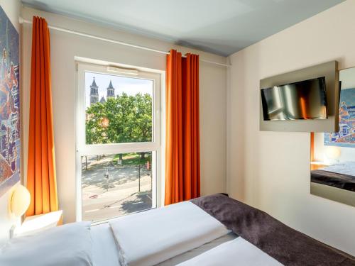 a bedroom with a large window with orange curtains at B&B HOTEL Magdeburg-City in Magdeburg