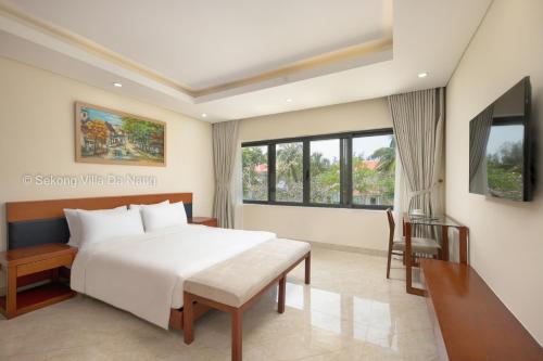 1 dormitorio con cama blanca, escritorio y ventana en Tran Beach Front Luxury Villa, en Da Nang