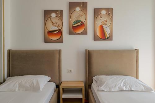 two beds in a room with three pictures on the wall at Hotel Summer in Sarandë