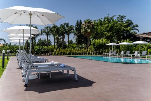 a row of lounge chairs with umbrellas next to a pool at Virdamuri - Etna Country Resort in Giarre