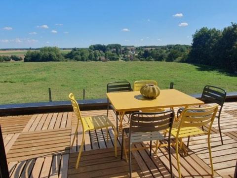 a table and chairs on a wooden deck with a field at Le pré en bulles in Lespesses