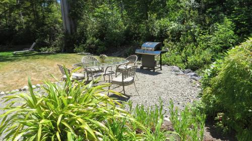 a table and chairs and a grill in a garden at Cobble Wood and Bird Sanctuary Guest Houses in Tofino