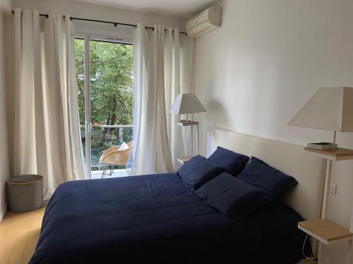een slaapkamer met een blauw bed en een groot raam bij Appartement 65m2 avec balcon in Neuilly-sur-Seine